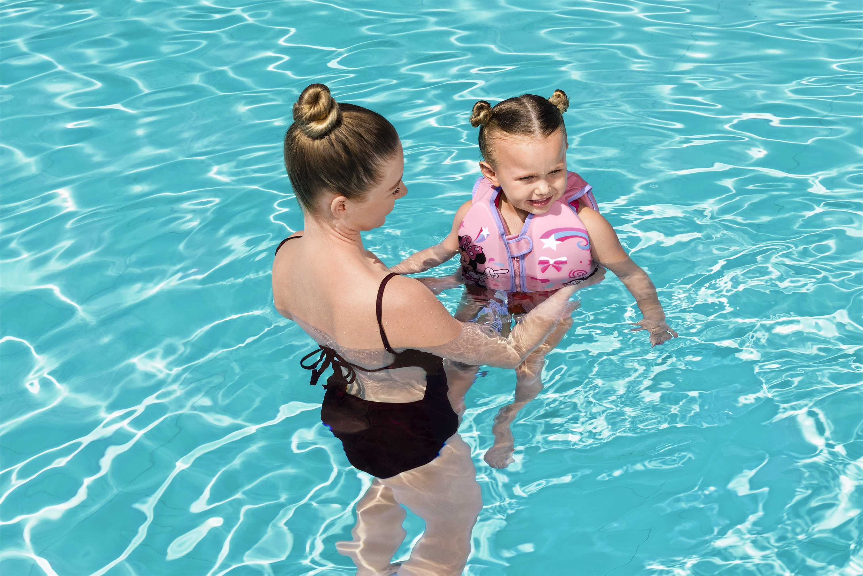 Donna in costume da bagno in piscina aiuta una bambina con gilet rosa.