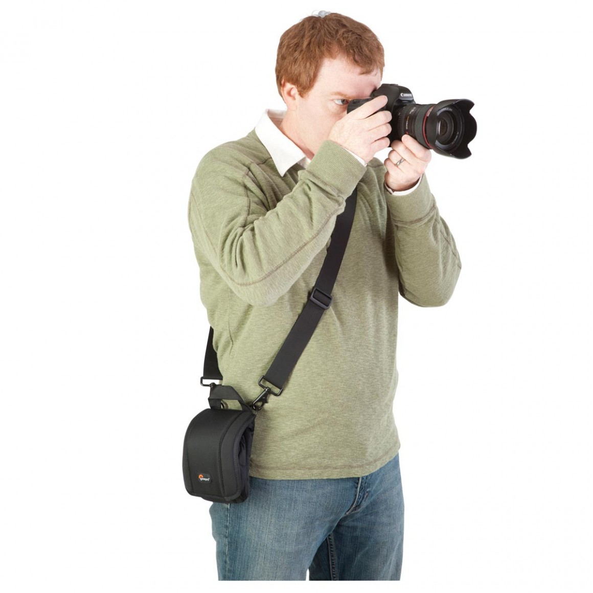 Ein Mann in einem grünen Hemd und Jeans fotografiert mit einer schwarzen Kamera und trägt einen schwarzen Riemen.