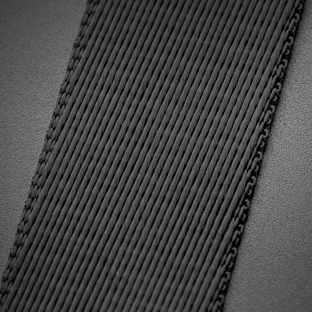 Zbliżenie czarnego, teksturowanego paska z przeszyciami na szarej powierzchni.