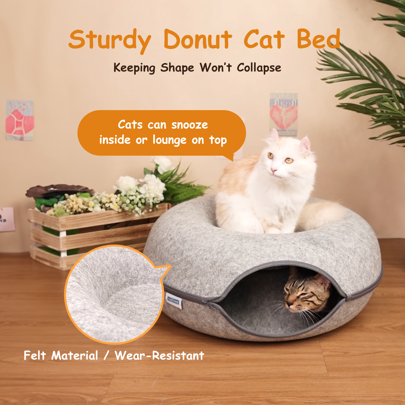 Una cama para gatos en forma de donut gris con dos gatos, uno dentro y otro encima.