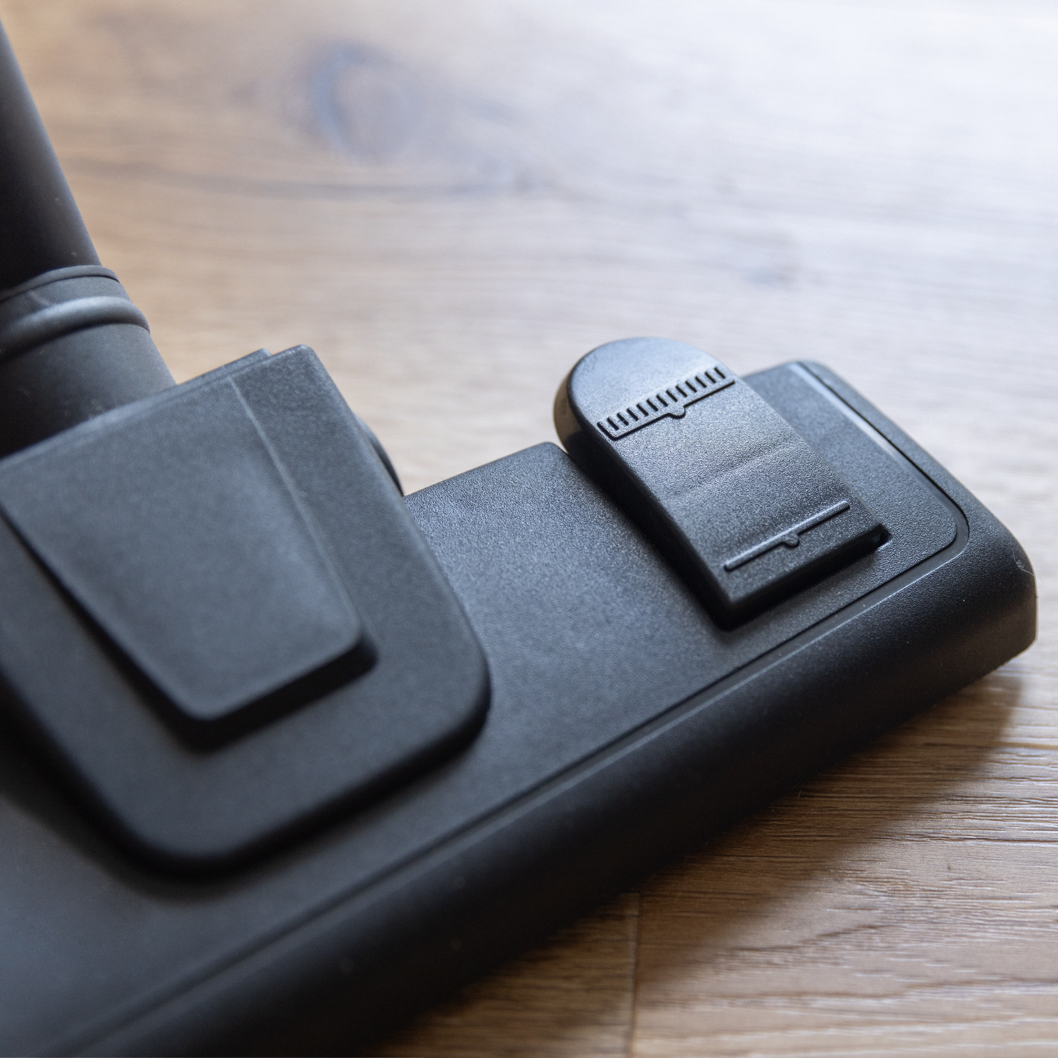 Black vacuum cleaner head on wooden floor. The floor is light brown.
