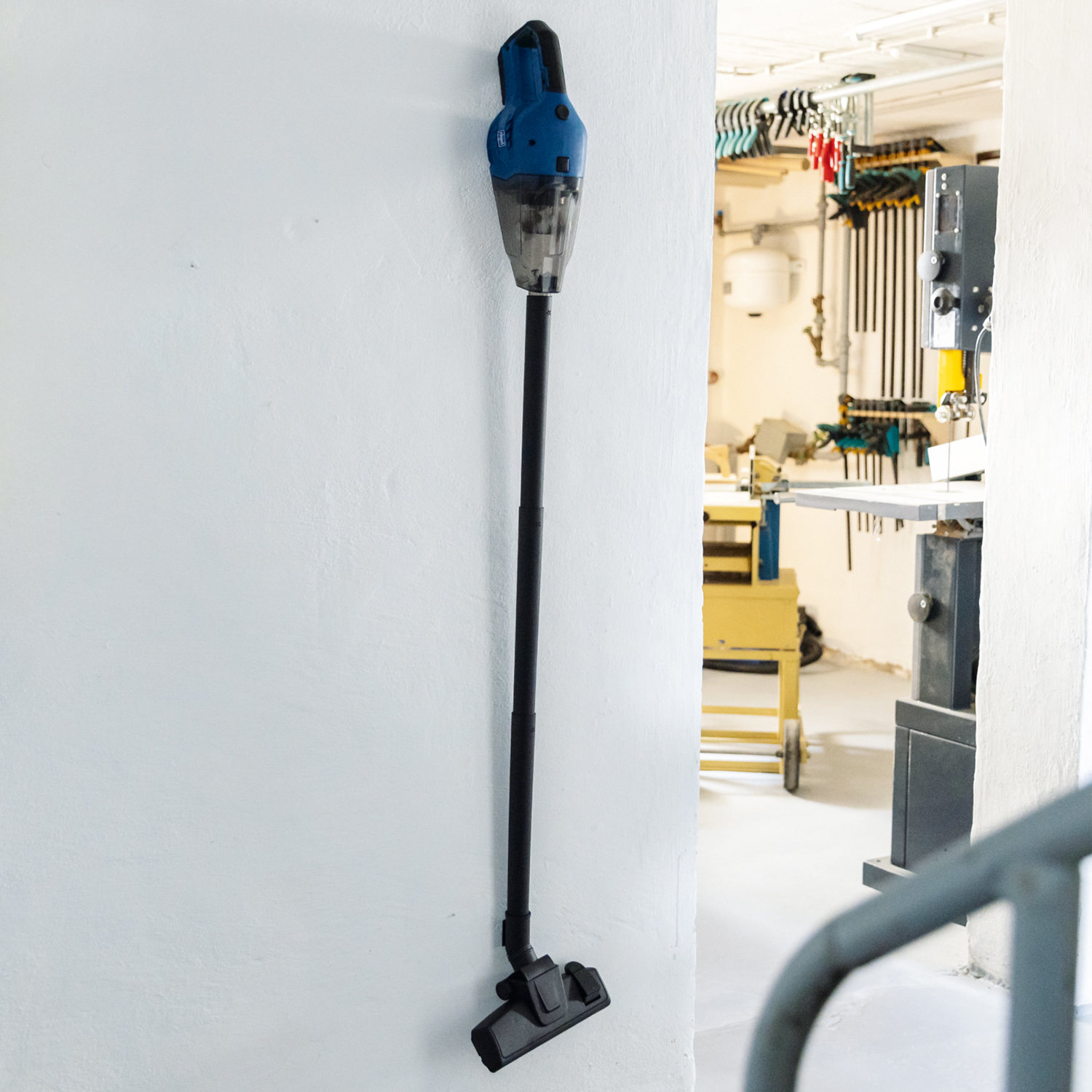 Blue and black cordless vacuum cleaner hangs on a white wall in a room. The room's background.
