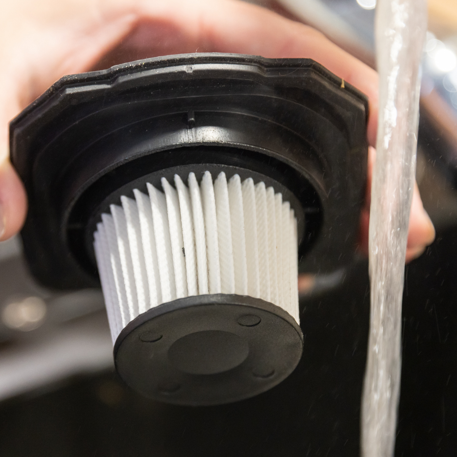 A vacuum filter being cleaned under running water. The filter is white and black.