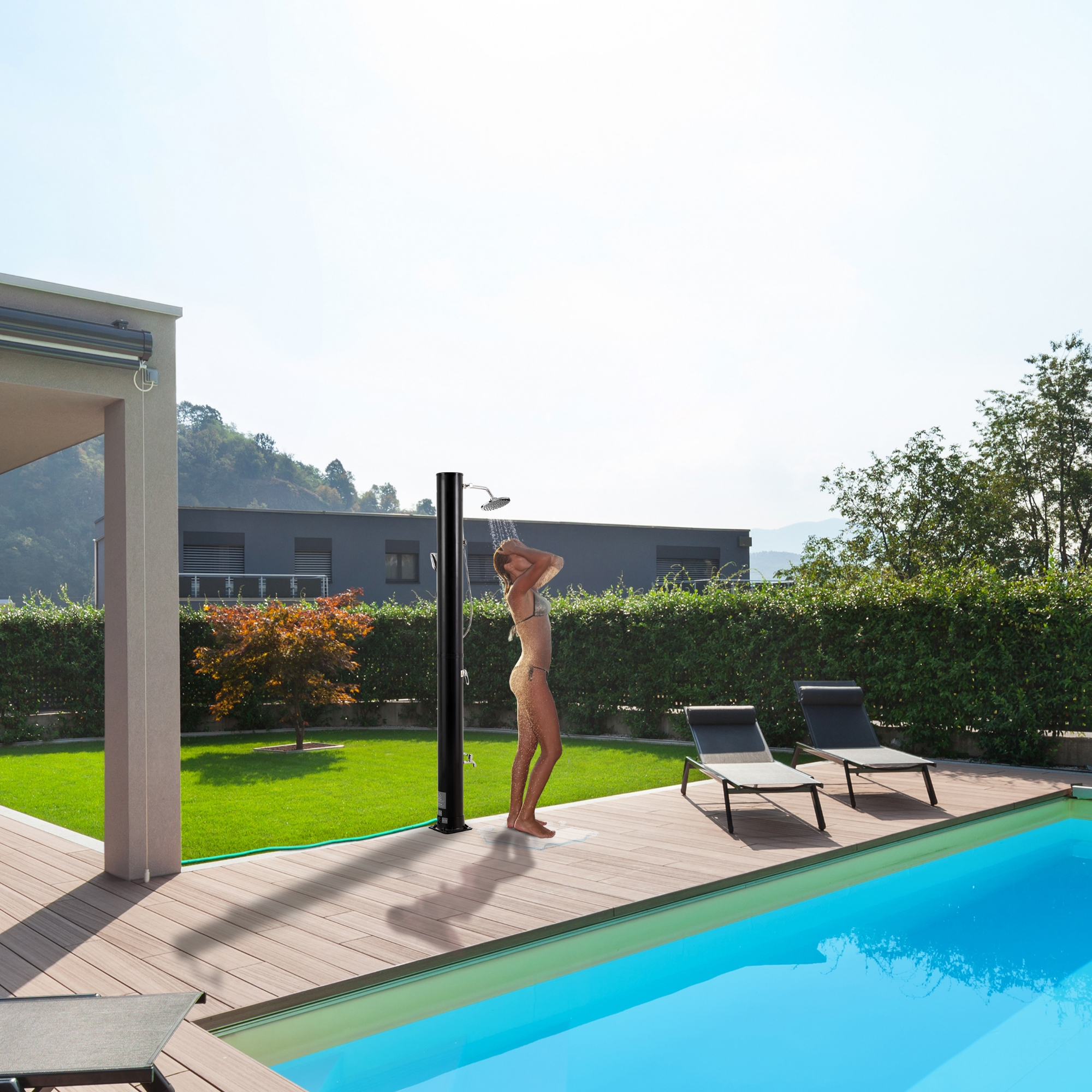 Frau duscht im Freien am Pool an einem sonnigen Tag. Grünes Gras, Bäume und ein Haus sind im Hintergrund.