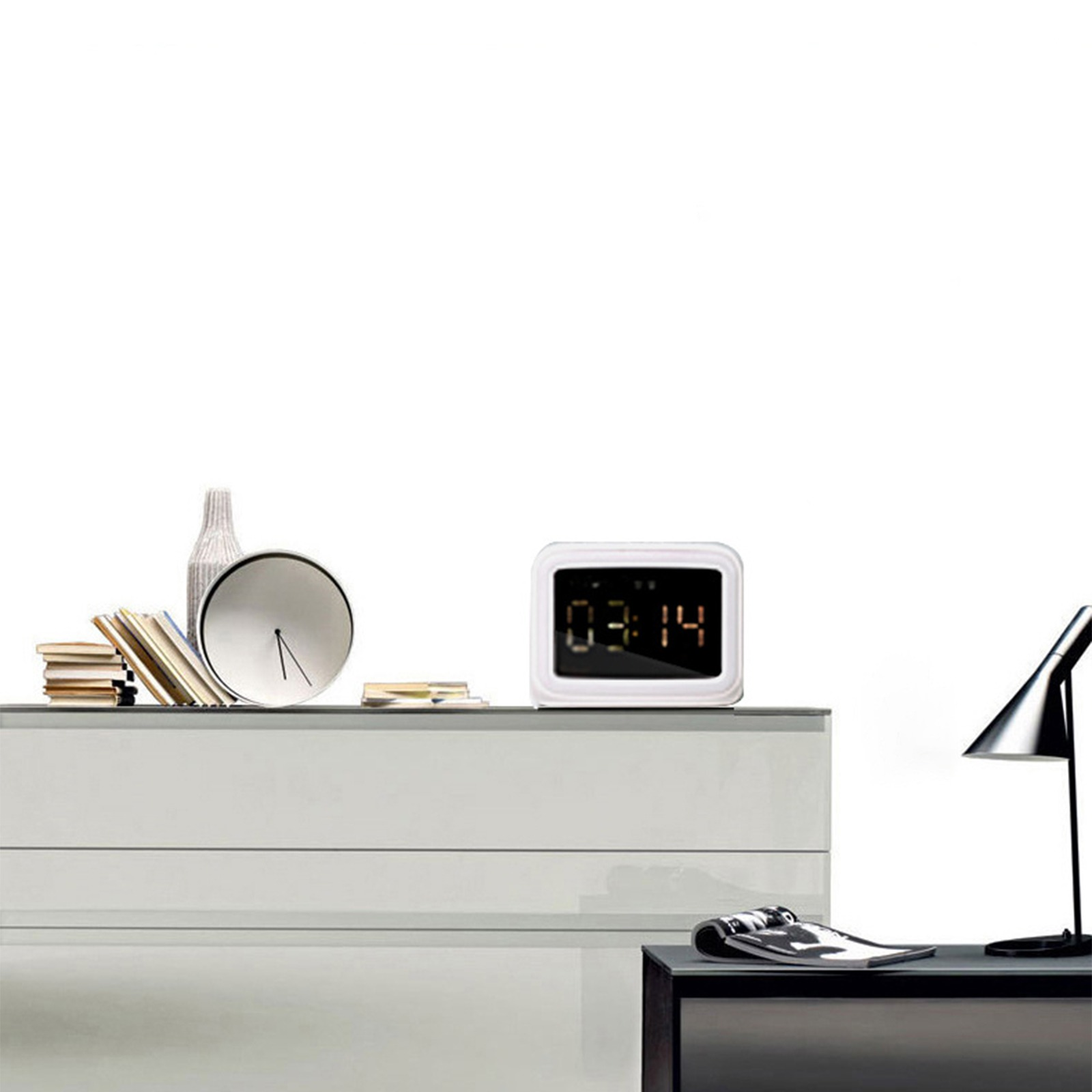 Eine weiße Kommode mit Uhr, Vase, Büchern und Lampe. Eine Digitaluhr zeigt die Zeit.