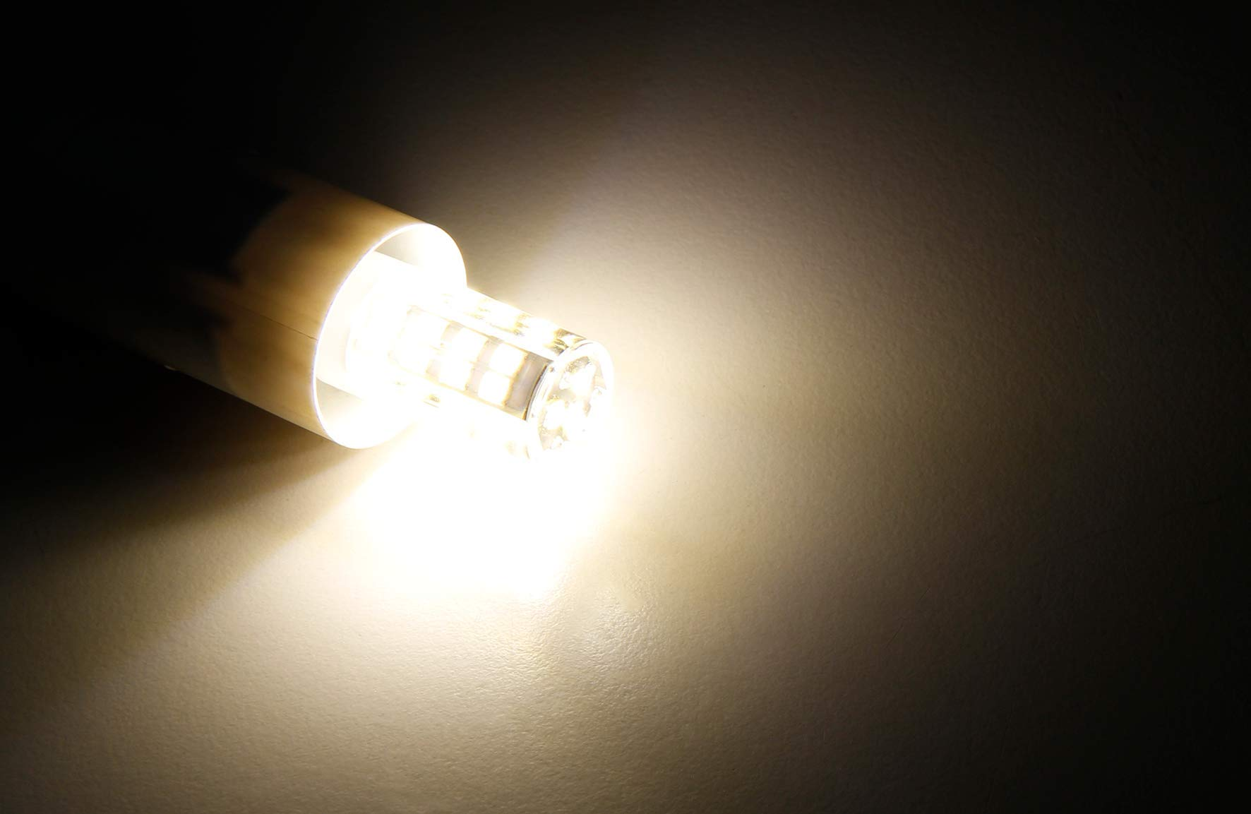 Eine leuchtende LED-Glühbirne in einem weißen Rohr. Das Licht ist warm. Dunkler Hintergrund.