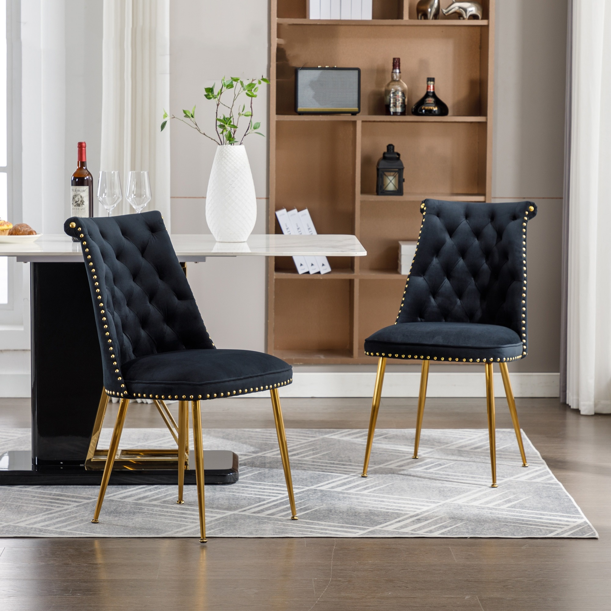 Zwei schwarze Samt-Esszimmerstühle mit goldenen Beinen und Nietenbesatz, neben einem Marmortisch.