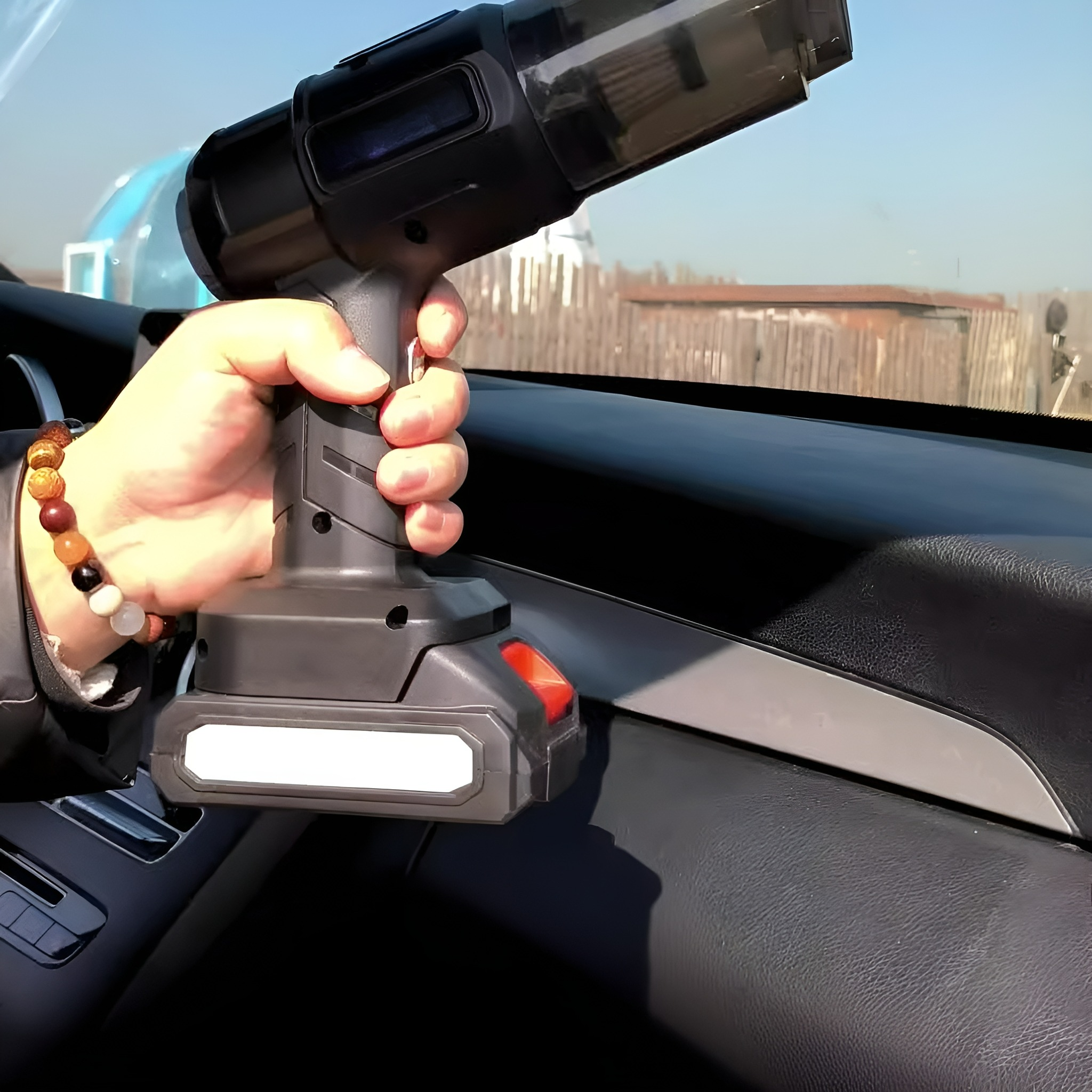 Eine Hand, die einen schwarzen und grauen kabellosen Staubsauger in einem Auto hält.