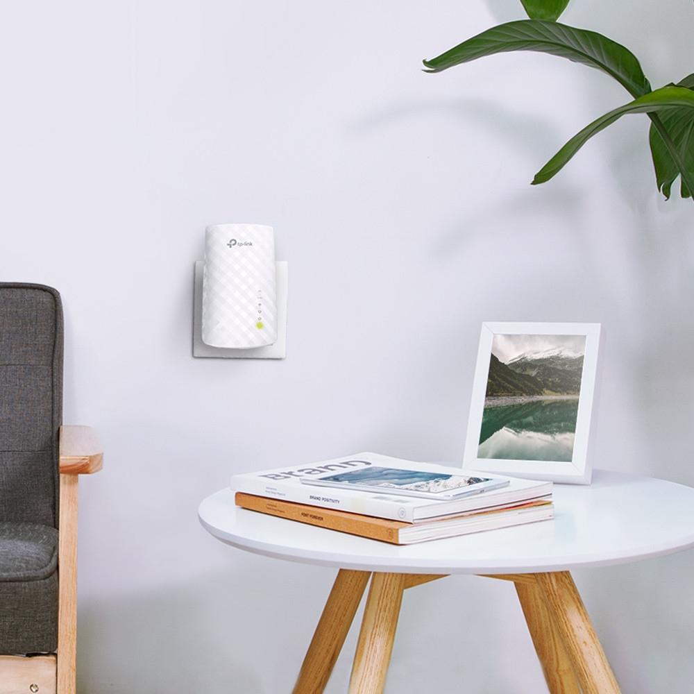 Ein weißer TP-Link WLAN-Repeater an der Wand. Bücher und ein gerahmtes Bild in der Nähe.