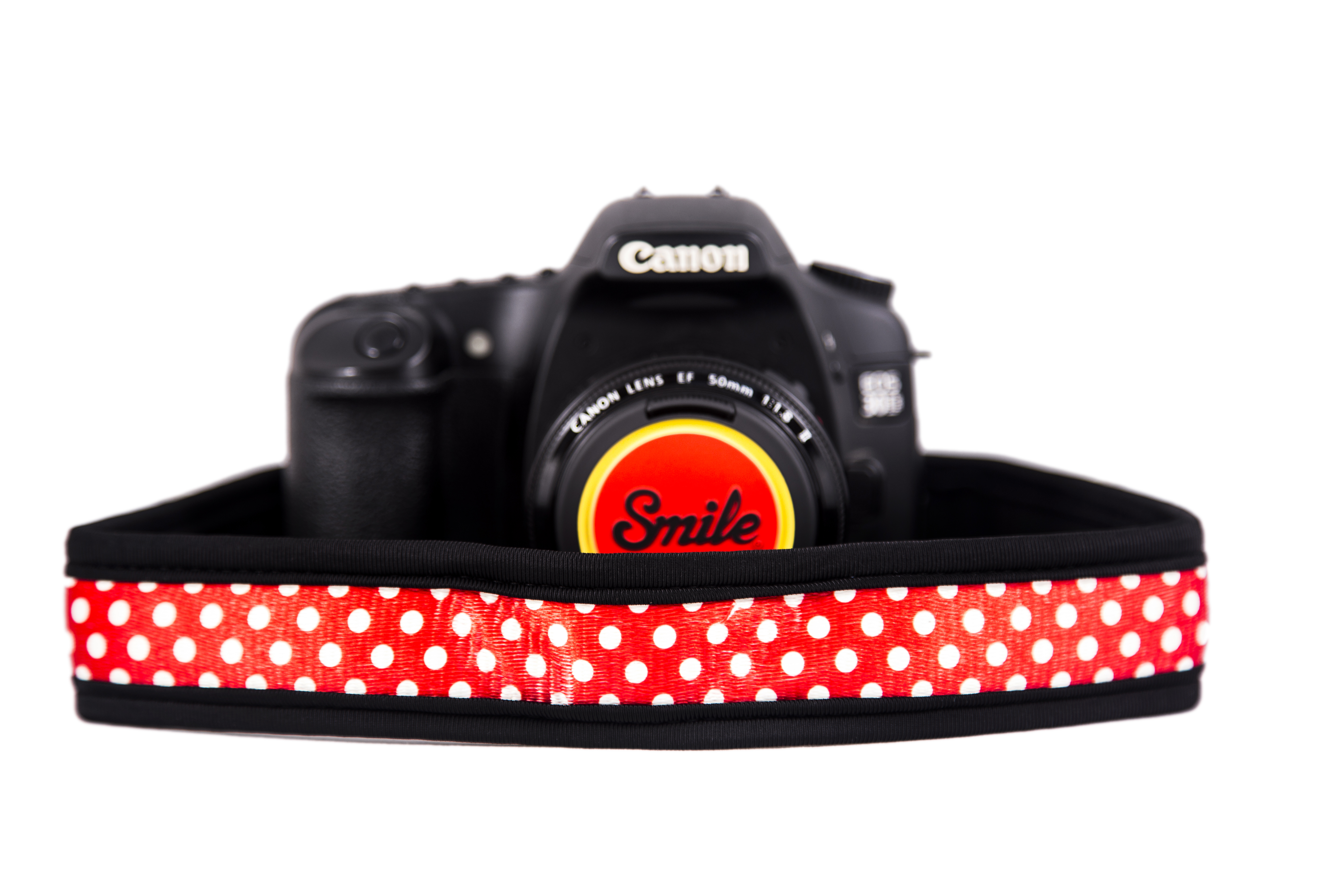 Una fotocamera con un cinturino a pois rossi e bianchi e un obiettivo con la scritta 'Smile'.