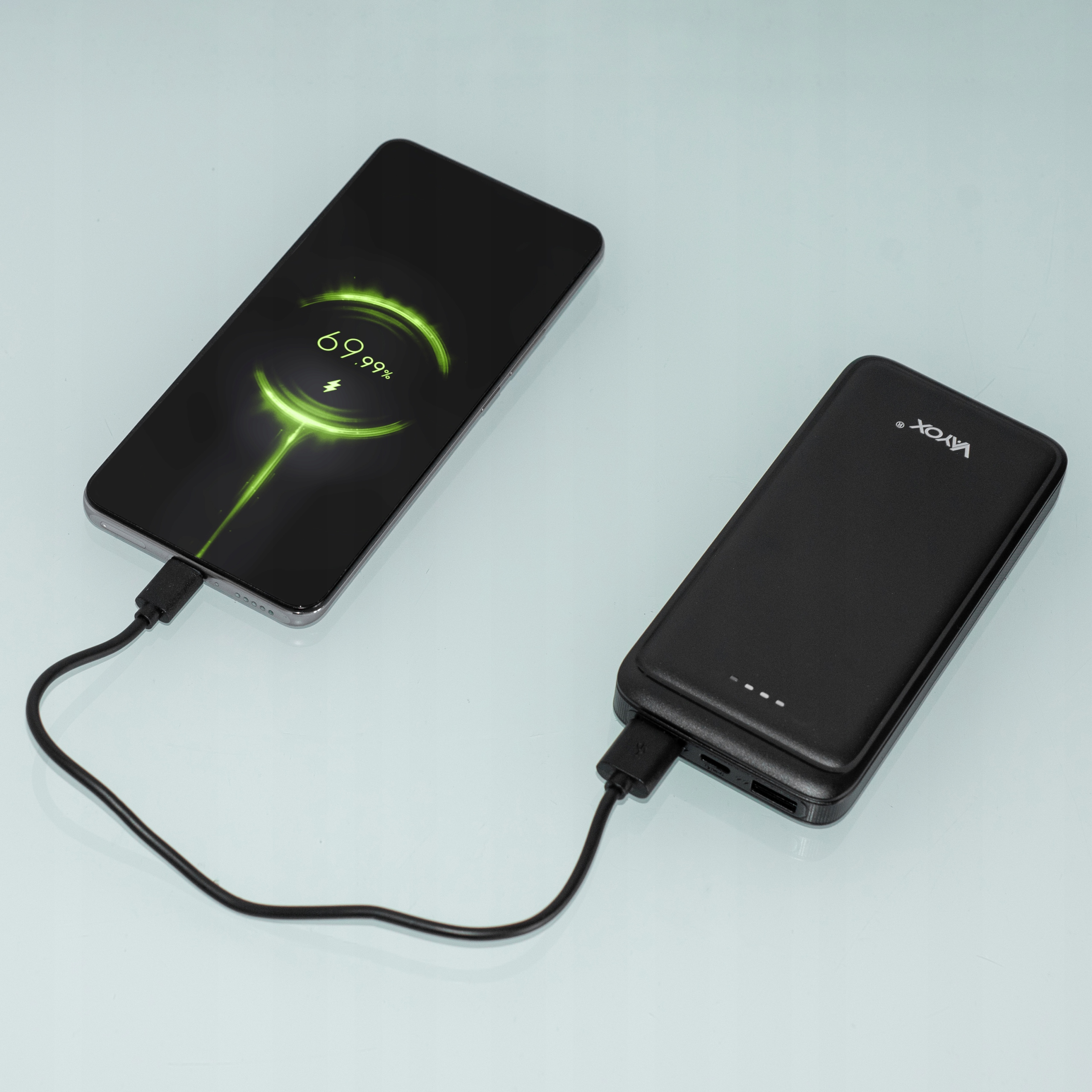 Telefon ładuje się z czarnego power banku. Ekran telefonu pokazuje 69,99% naładowania.