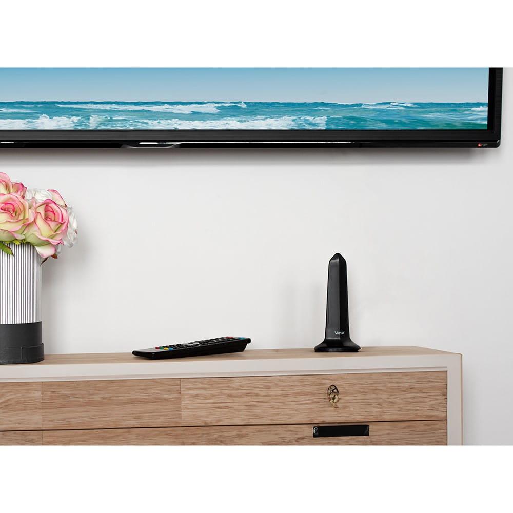 Antena na drewnianej szafce. W tle telewizor i wazon z kwiatami.