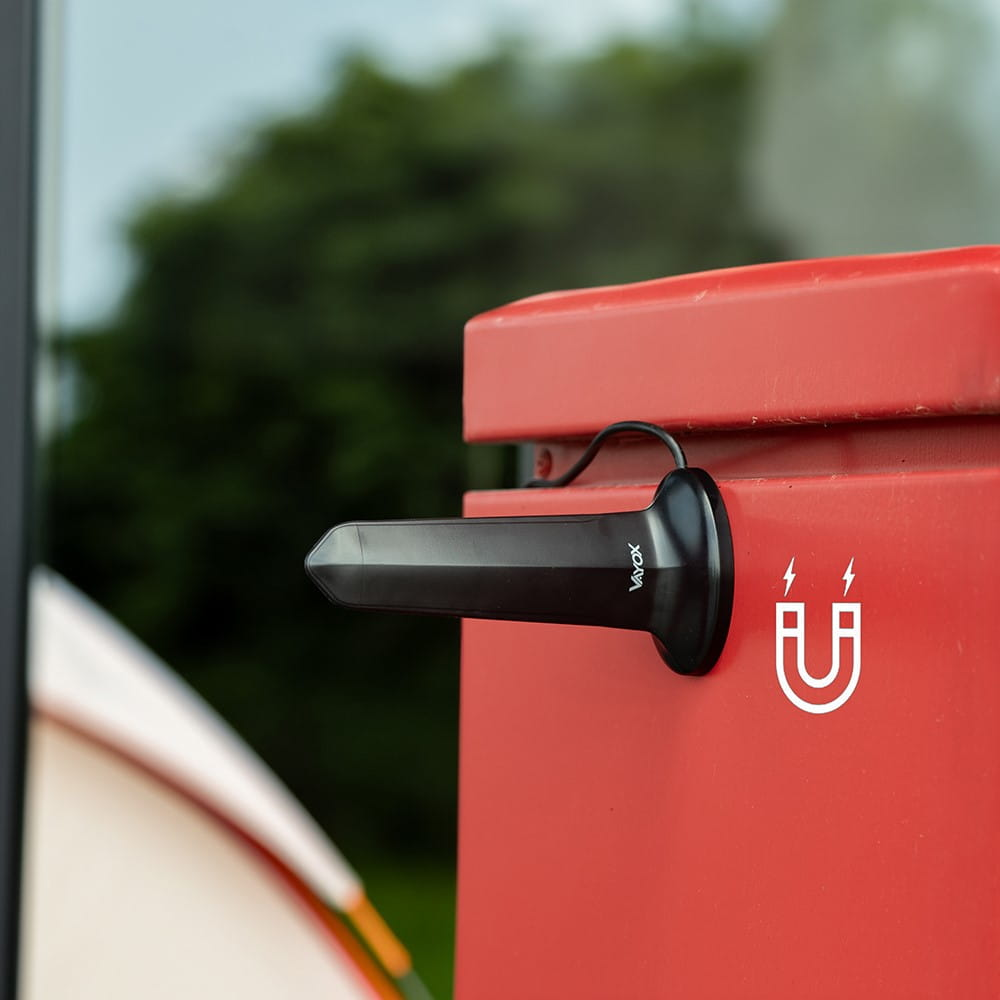 Czarna antena przymocowana do czerwonego obiektu z symbolem magnesu. Zielone drzewa w tle.