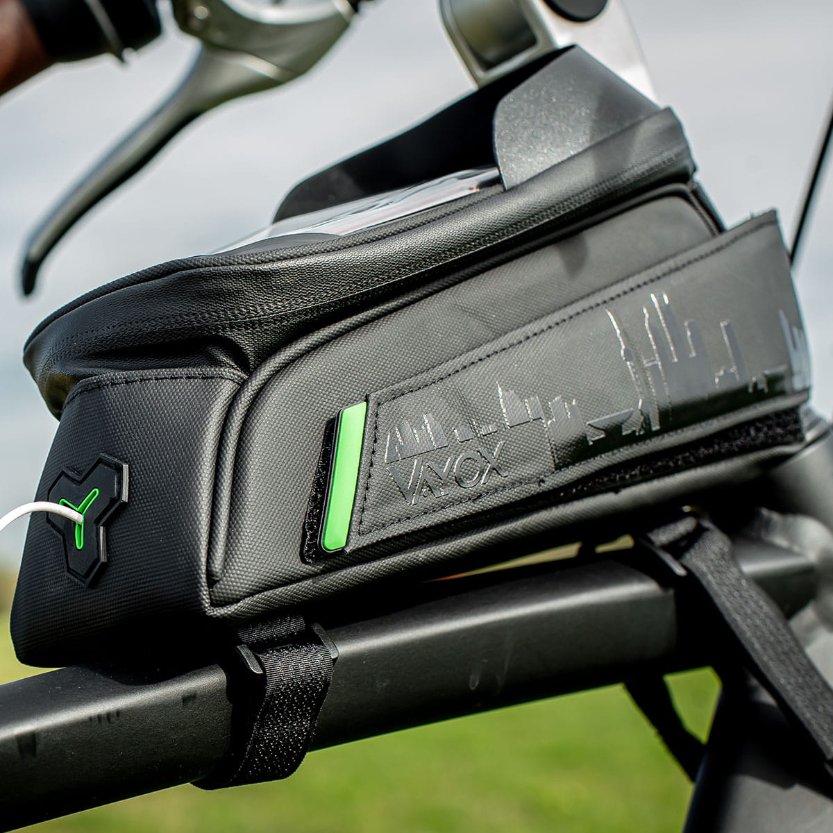 Torba rowerowa przymocowana do roweru. Czarna torba z zielonymi akcentami, przymocowana do kierownicy roweru. Logo panoramy miasta.