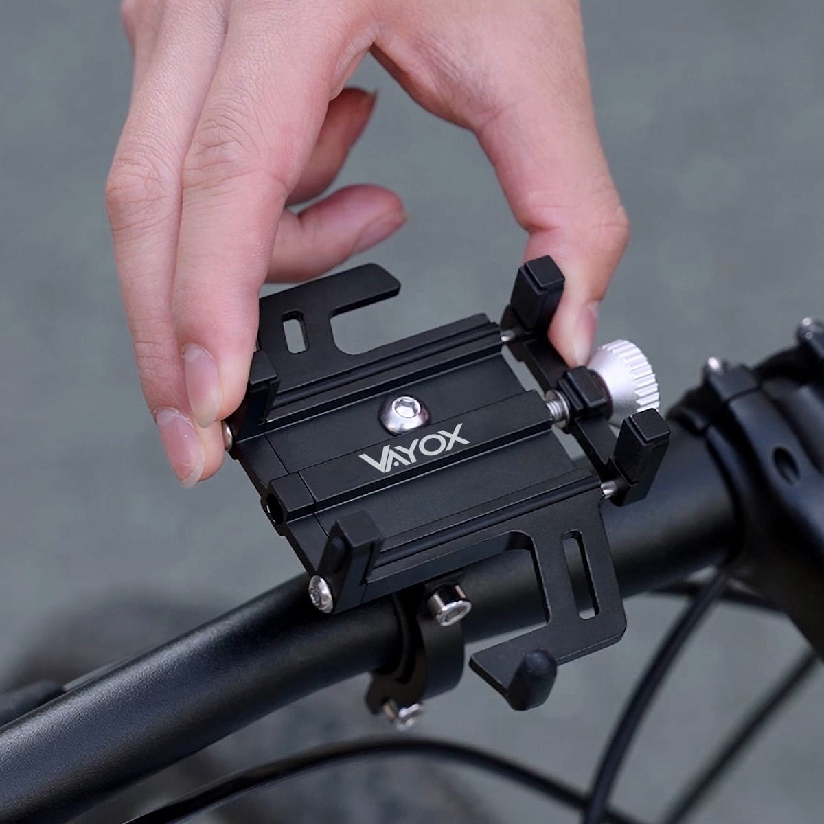 Czarny uchwyt na telefon zamontowany na kierownicy roweru. Ręka go reguluje.