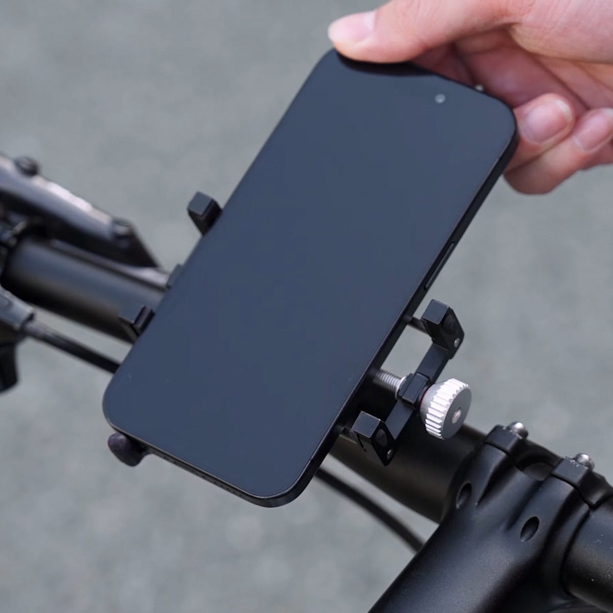 Ręka umieszczająca czarny smartfon w uchwycie na telefon do roweru.