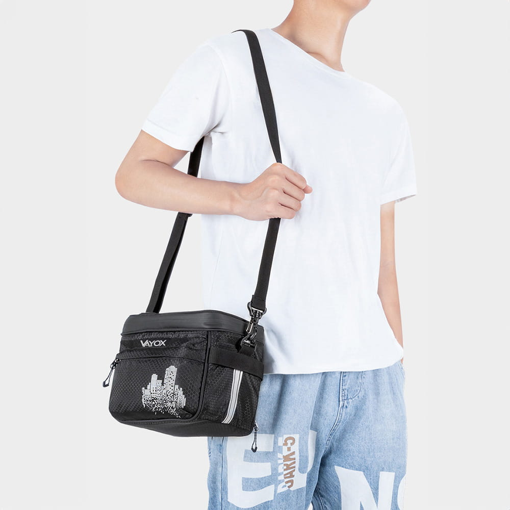 Mężczyzna noszący czarną torbę na ramię z miejskim motywem, w swobodnej scenerii.