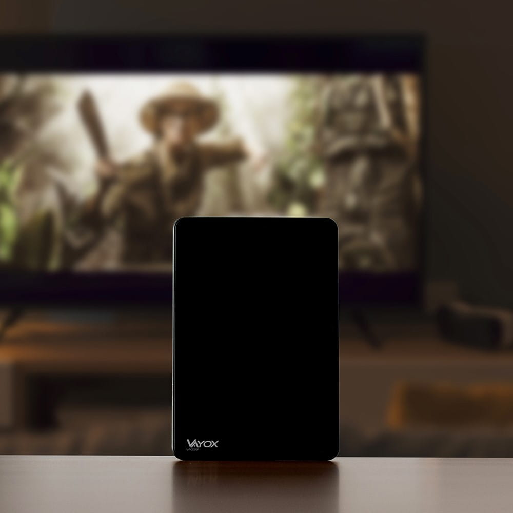 Czarna antena na stole, z rozmytym tłem salonu i telewizora.