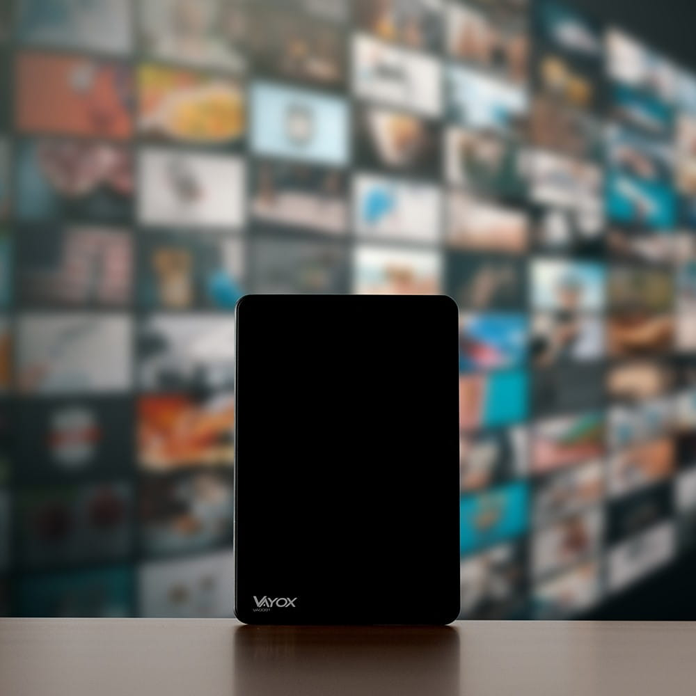 Czarny tablet na stole, z rozmytym tłem ekranów wyświetlających różne treści.