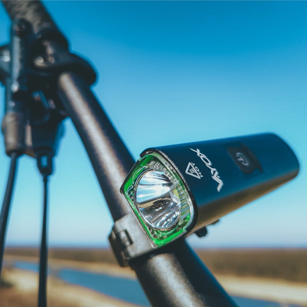 Czarna lampa rowerowa zamontowana na kierownicy roweru, z rozmytym tłem natury.