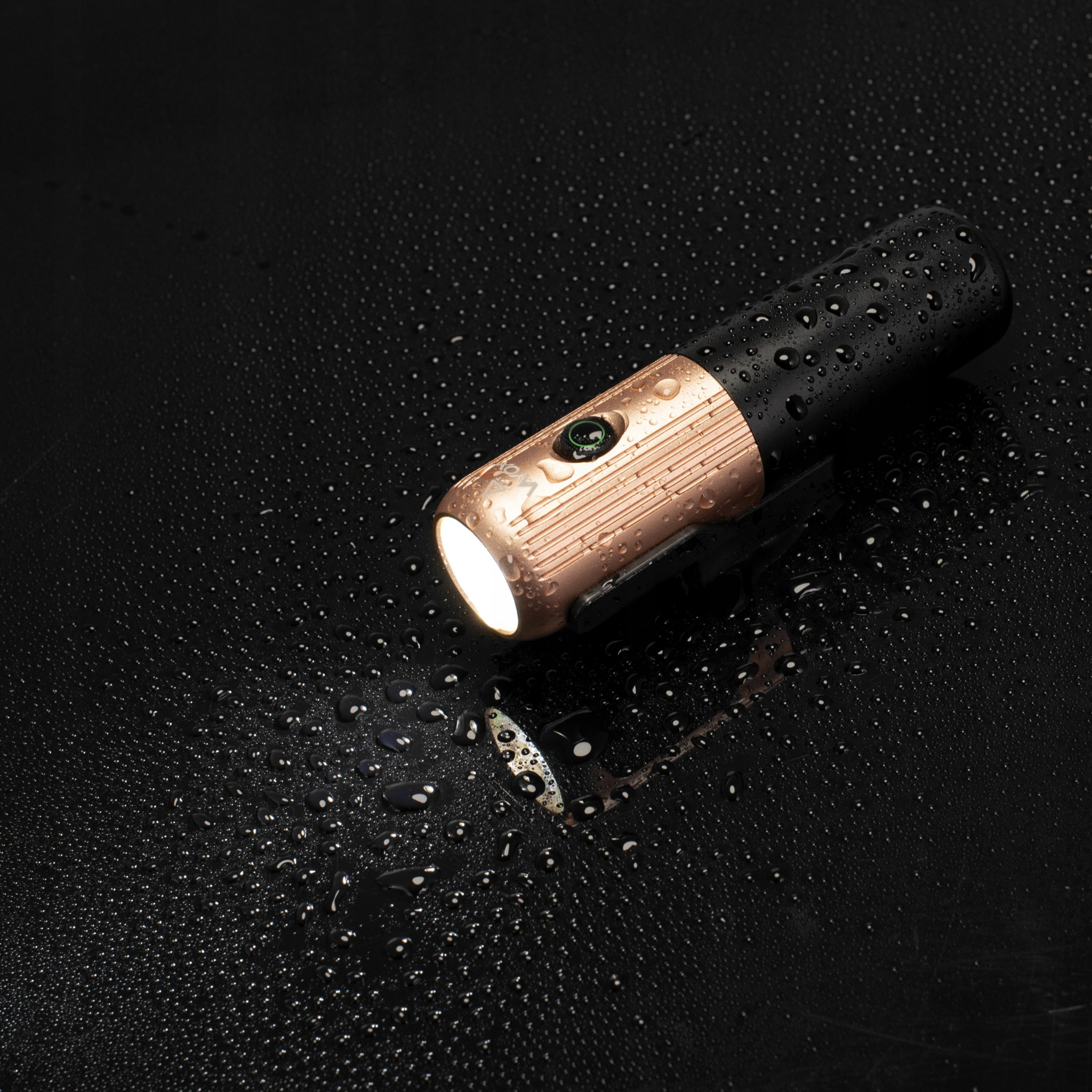 Latarka z mokrą powierzchnią. Złota i czarna, z podświetloną wiązką na ciemnym tle.