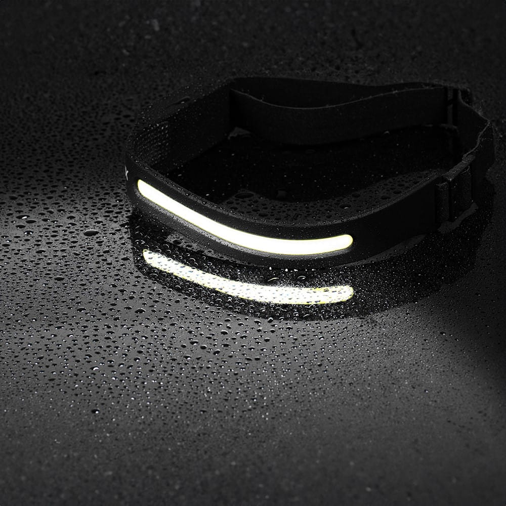 Czarna lampa czołowa na czarnej powierzchni z kroplami wody, światło świeci.