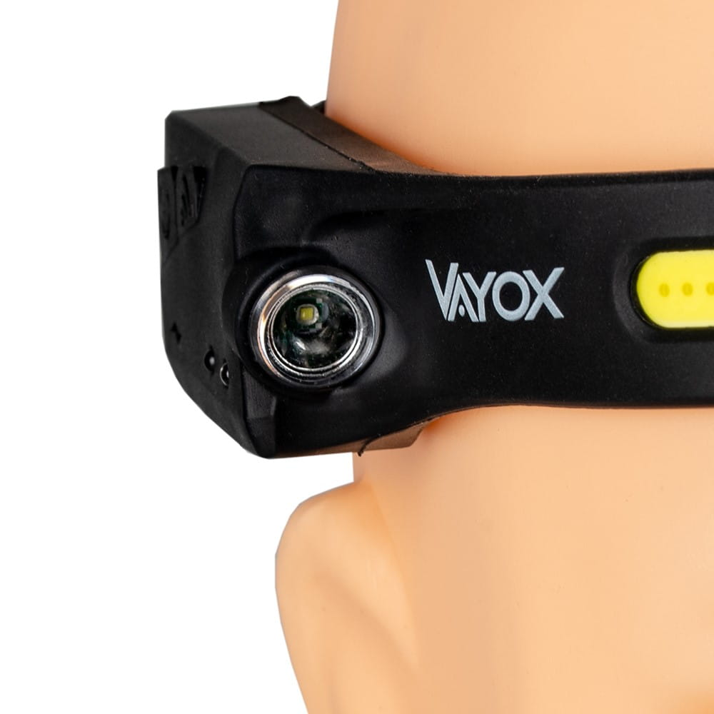 Zbliżenie czarnej lampy czołowej, ze słowem "VAYOX" i światłem z niej wychodzącym.