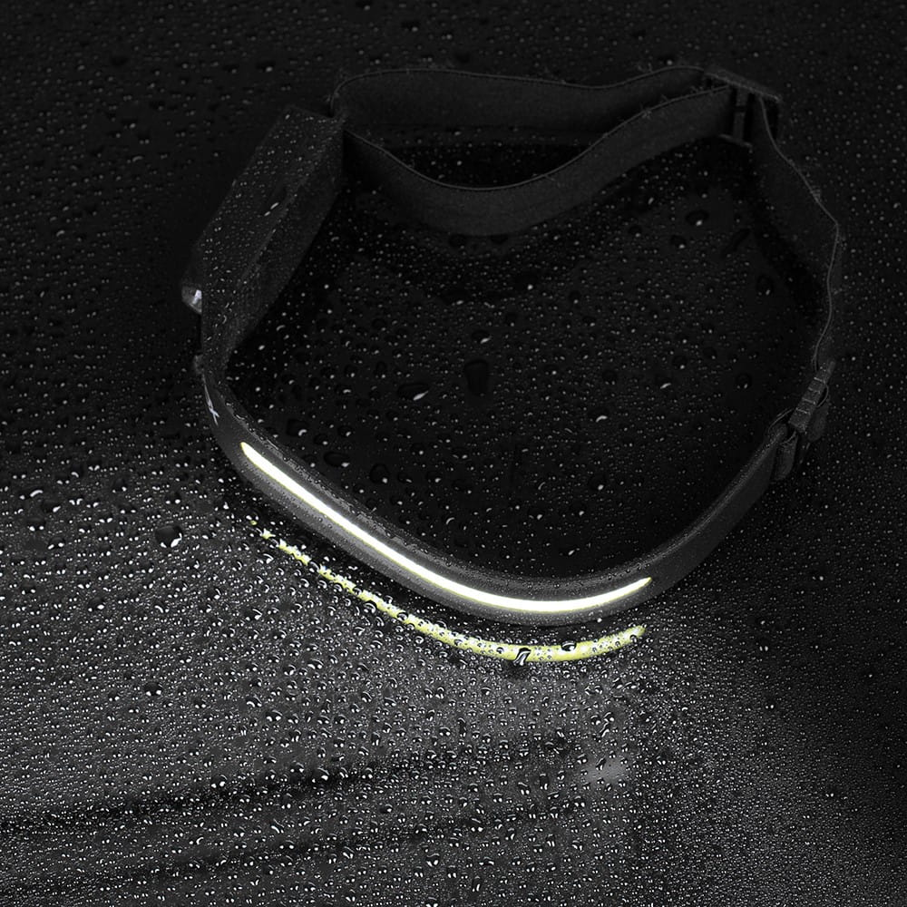 Latarka czołowa na mokrej czarnej powierzchni. Światło jest włączone. Rozrzucone krople wody.