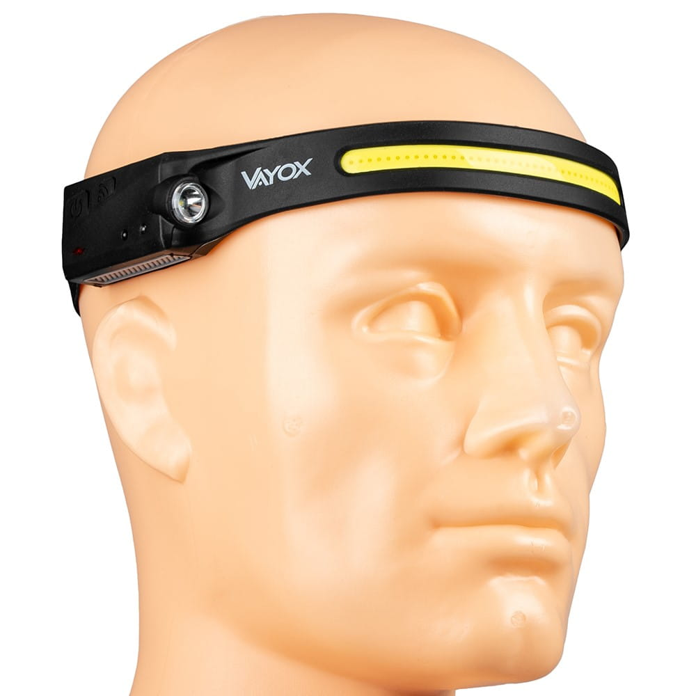 Manekin noszący czarną lampę czołową z napisem "VAYOX", emitującą światło.