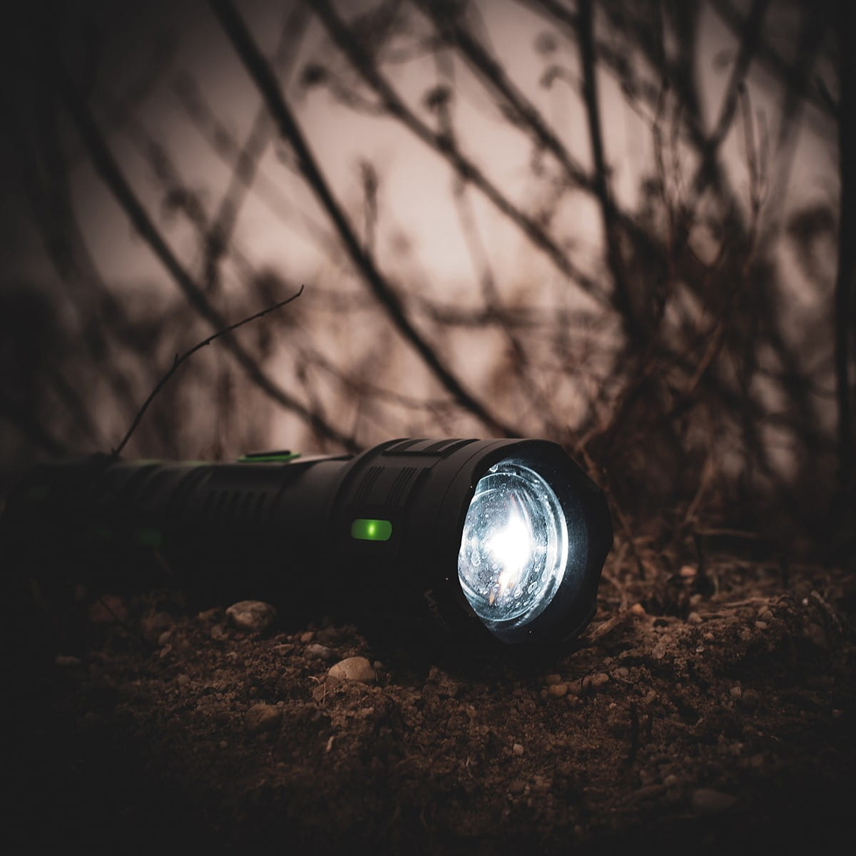 Czarna latarka na ziemi, soczewka oświetlona, otoczona ciemnym listowiem.