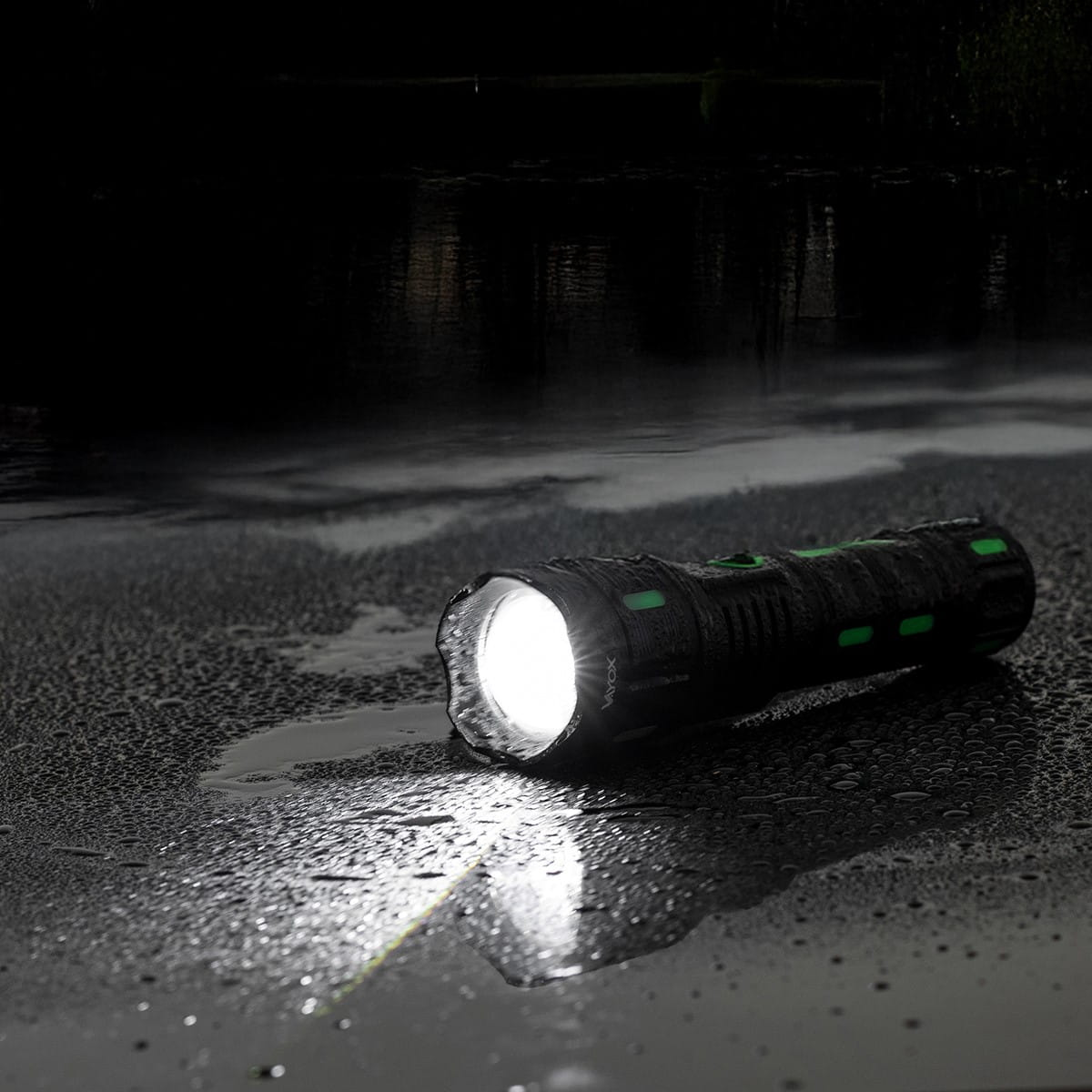 Czarna latarka na mokrej powierzchni, promień światła widoczny na ciemnym tle.