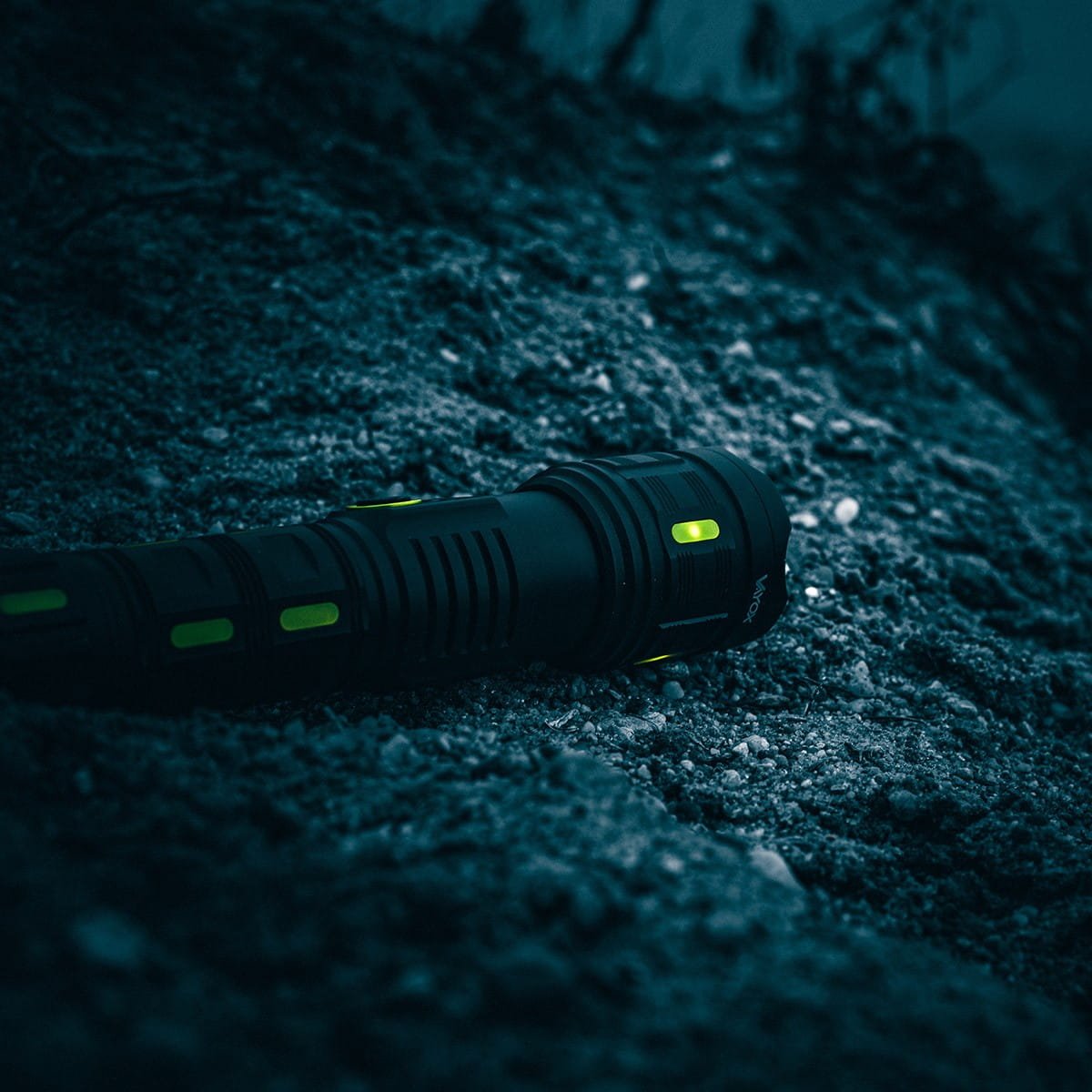 Czarna latarka na ciemnym, skalistym podłożu. Zielone światła są podświetlone z boku.