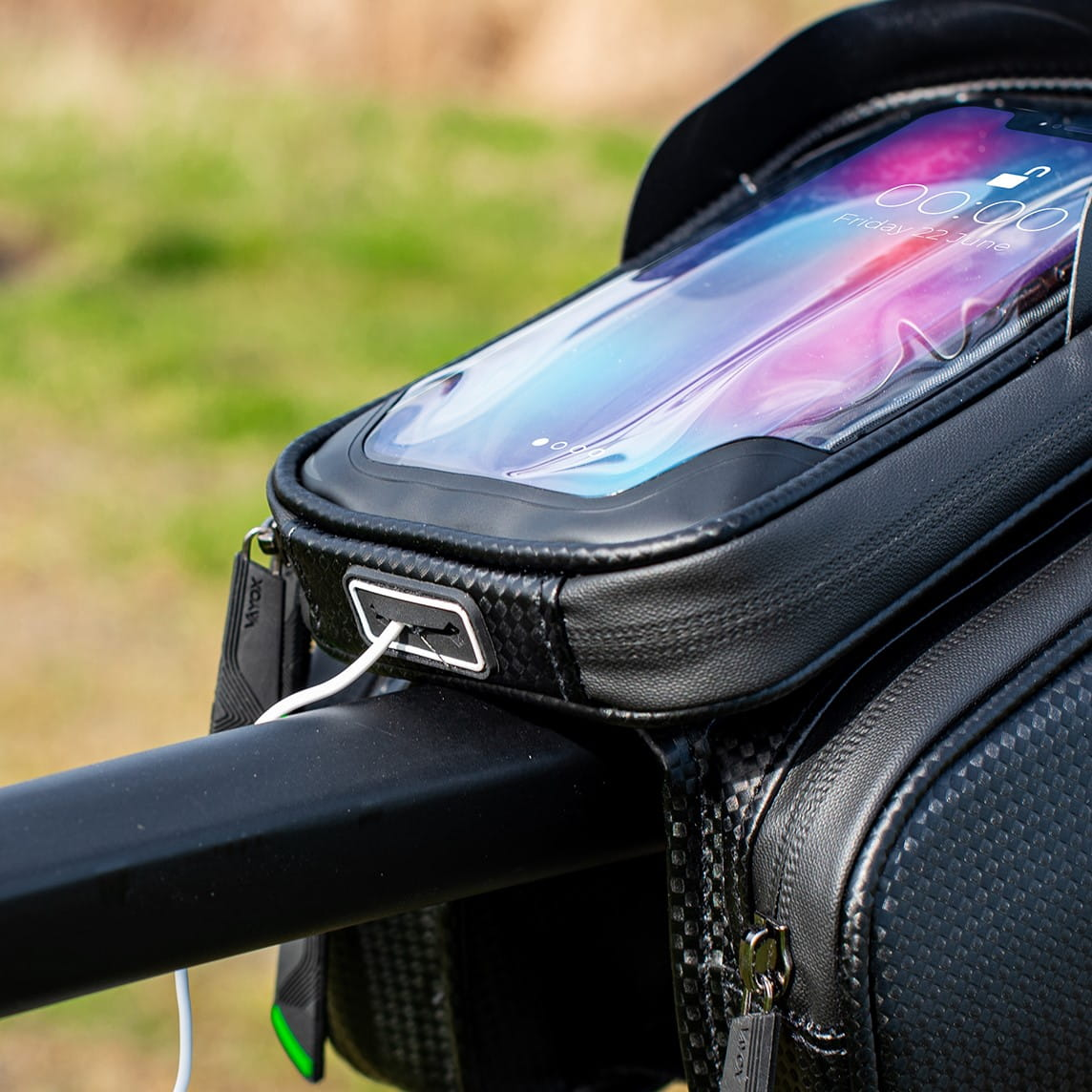 Torba rowerowa zamontowana na kierownicy z widocznym telefonem, kablem do ładowania i czarnym drążkiem.