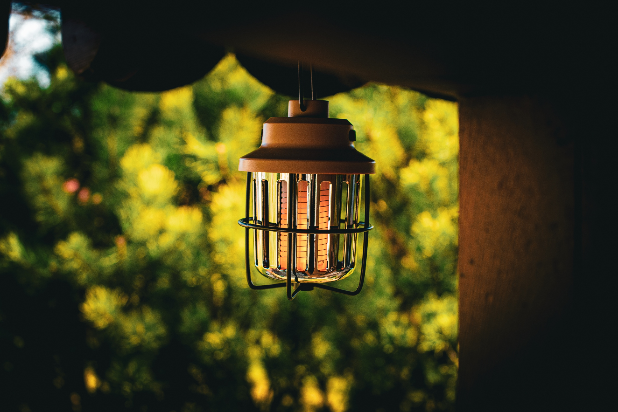 Beżowa i czarna latarnia wisząca na drewnianej konstrukcji.