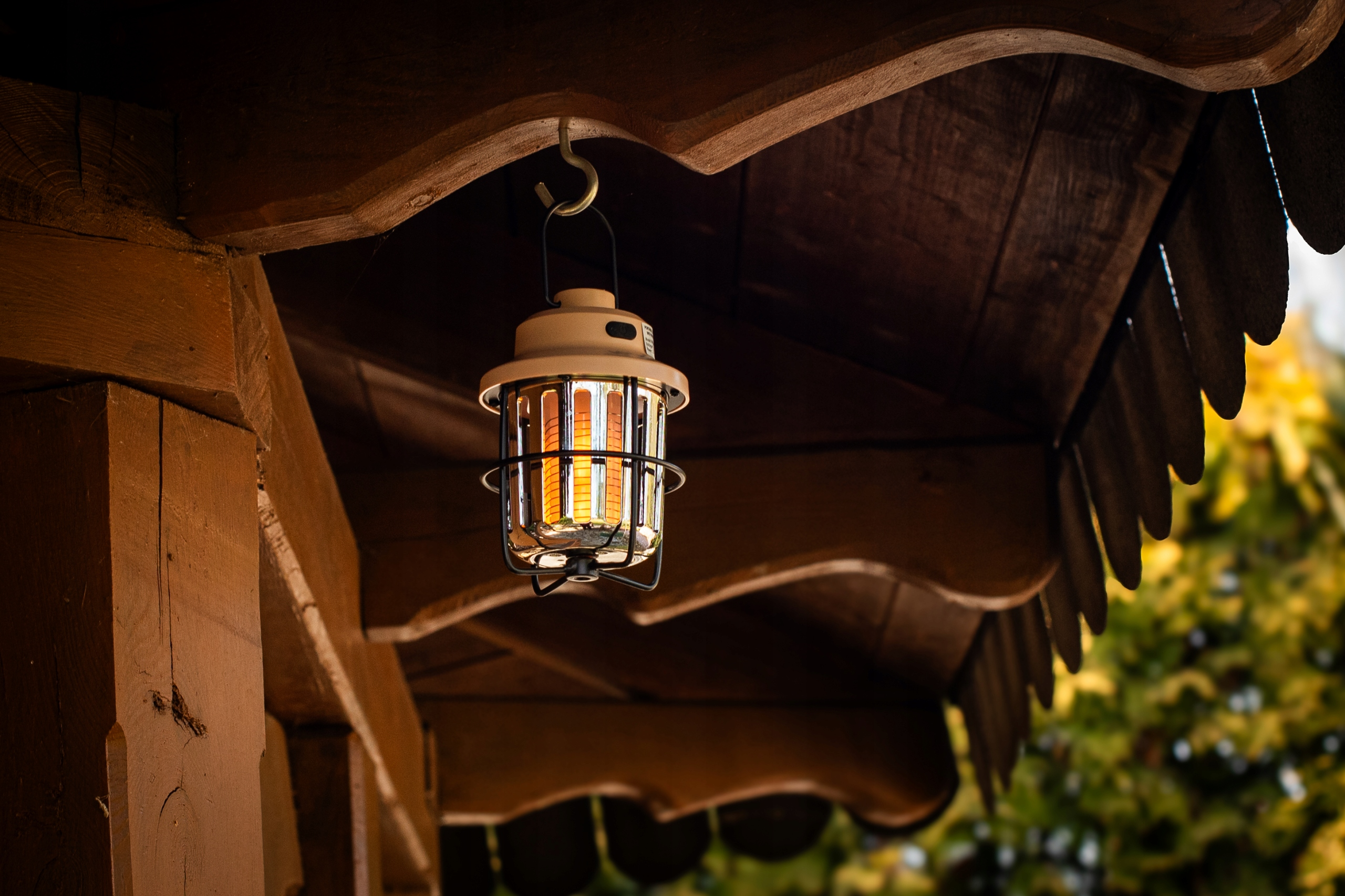 Beżowa latarnia zawieszona na haczyku na drewnianej konstrukcji.
