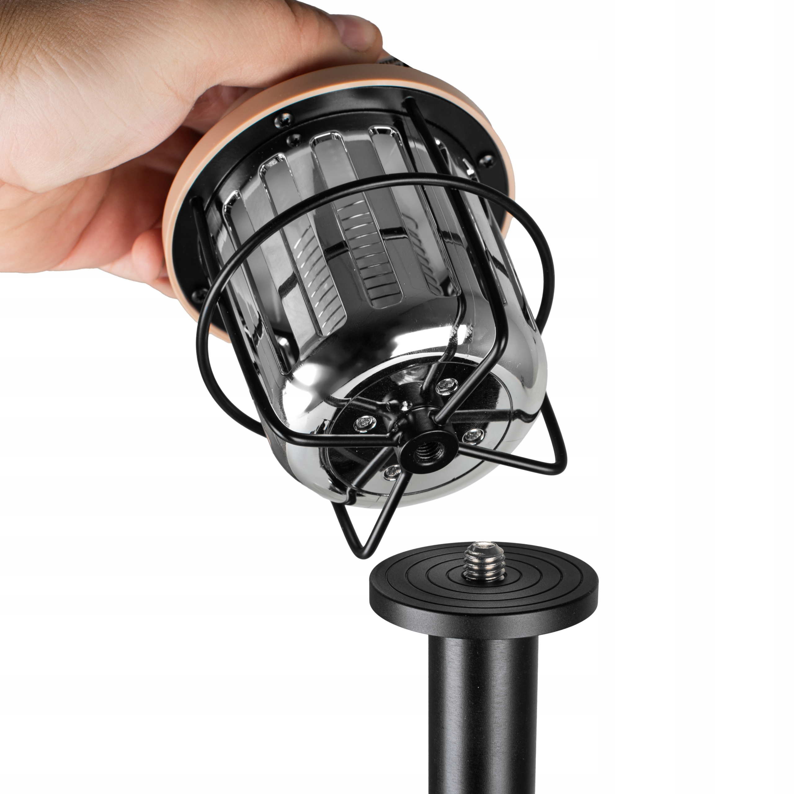 Ręka trzymająca beżową latarnię z czarną klatką nad stojakiem.