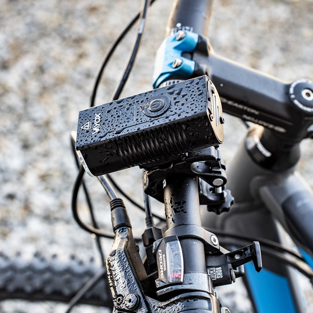 Czarne światło rowerowe zamontowane na kierownicy, z kroplami wody.