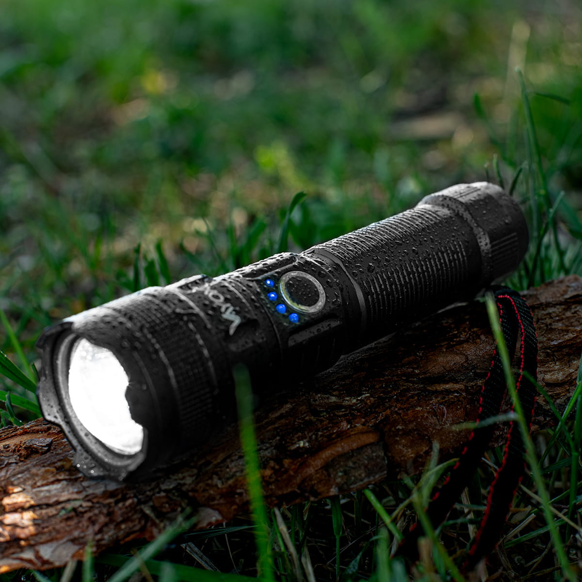 Czarna latarka Vayox na pniu, z zieloną trawą w tle, światło włączone.