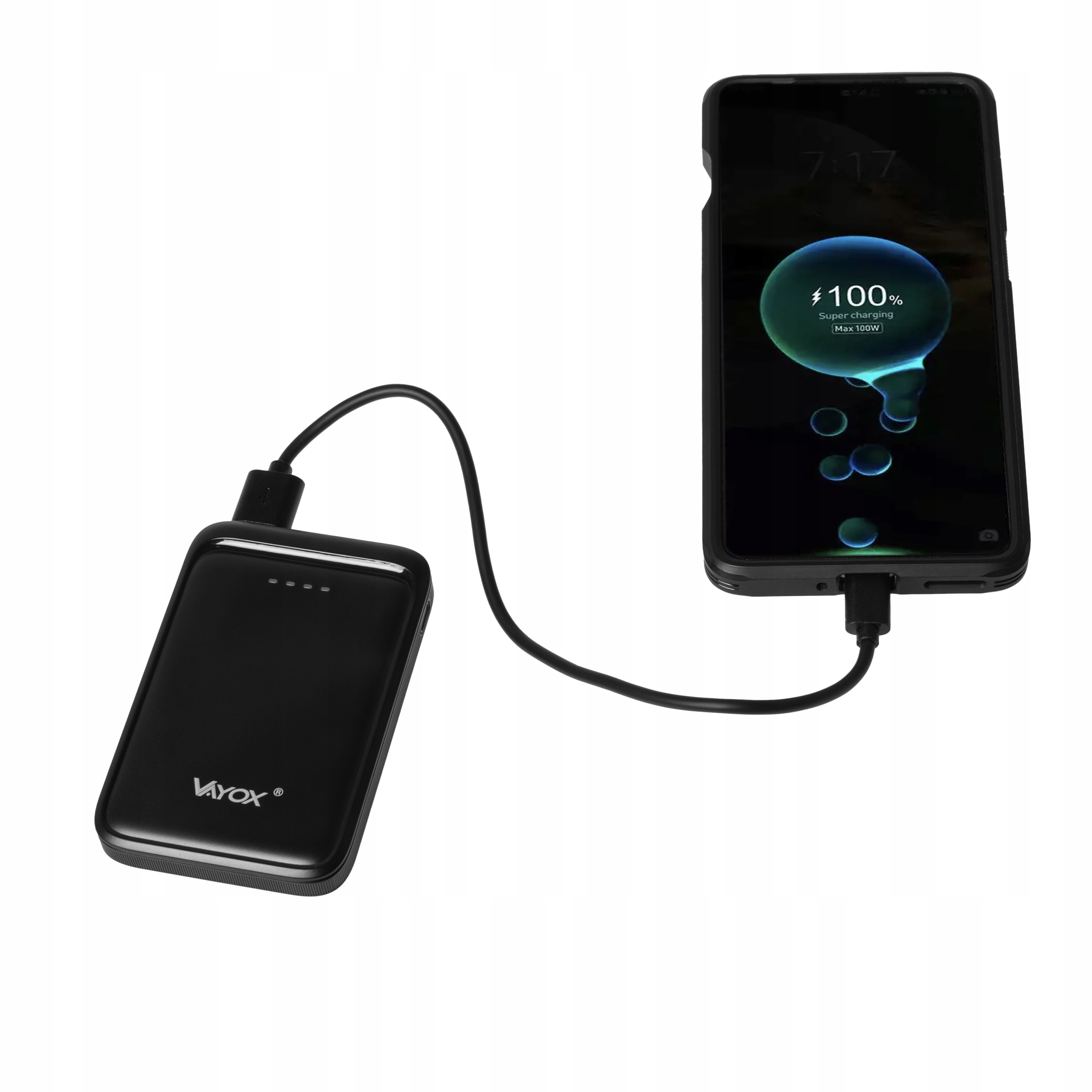 Czarny power bank ładujący smartfona. Telefon pokazuje 100% naładowania. Oba leżą na drewnianej powierzchni.