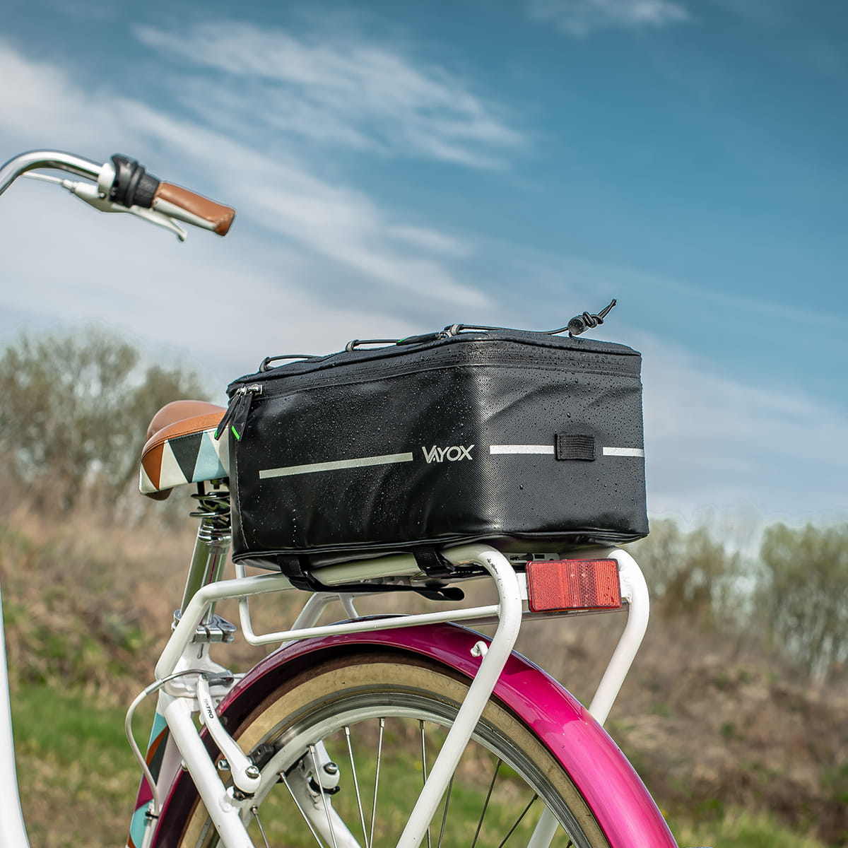 Czarna torba rowerowa zamontowana na bagażniku, z błękitnym niebem w tle.