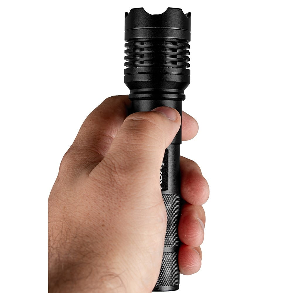 Dłoń trzyma czarną latarkę. Ma teksturowany uchwyt i czarną głowicę.