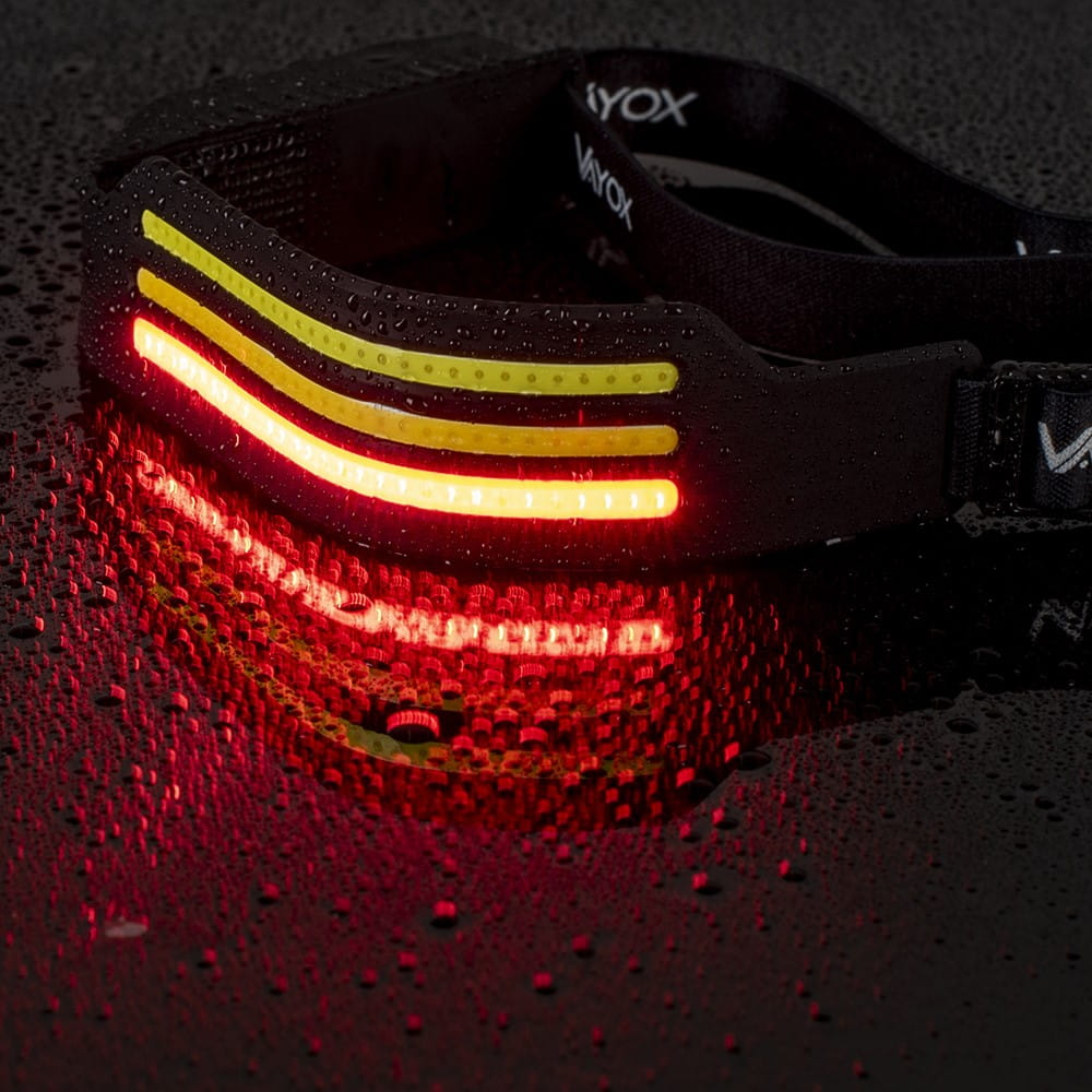 Czarna latarka czołowa z czerwonymi i żółtymi światłami. Krople wody na czarnej powierzchni.