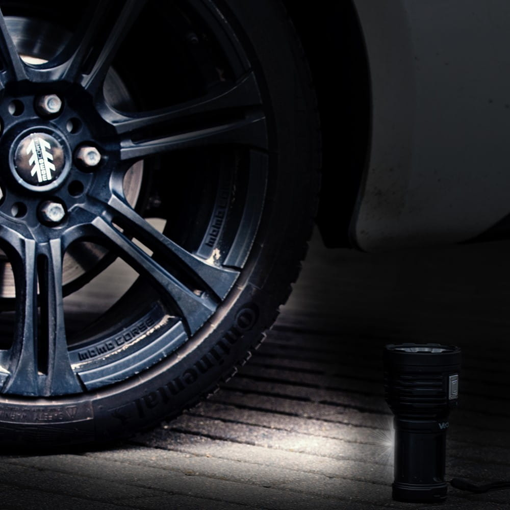 Czarna latarka oświetla ziemię obok koła samochodu.