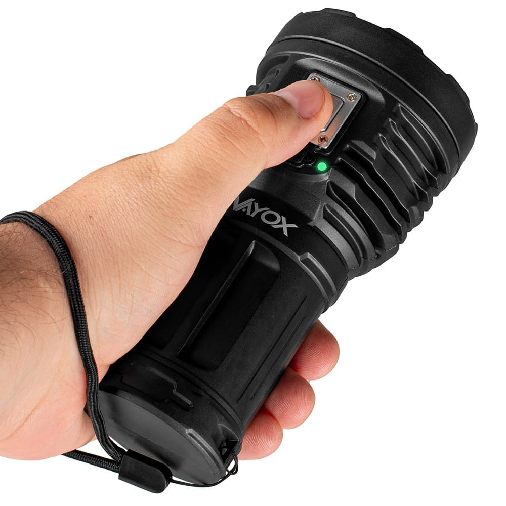 Ręka trzyma czarną latarkę Vayox, naciska przycisk, z zielonym światłem.