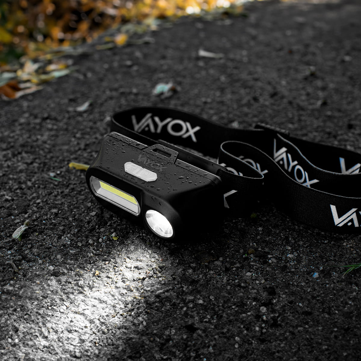 Czarna lampa czołowa na szarej powierzchni, z zapalonym białym światłem. Zbliżenie.