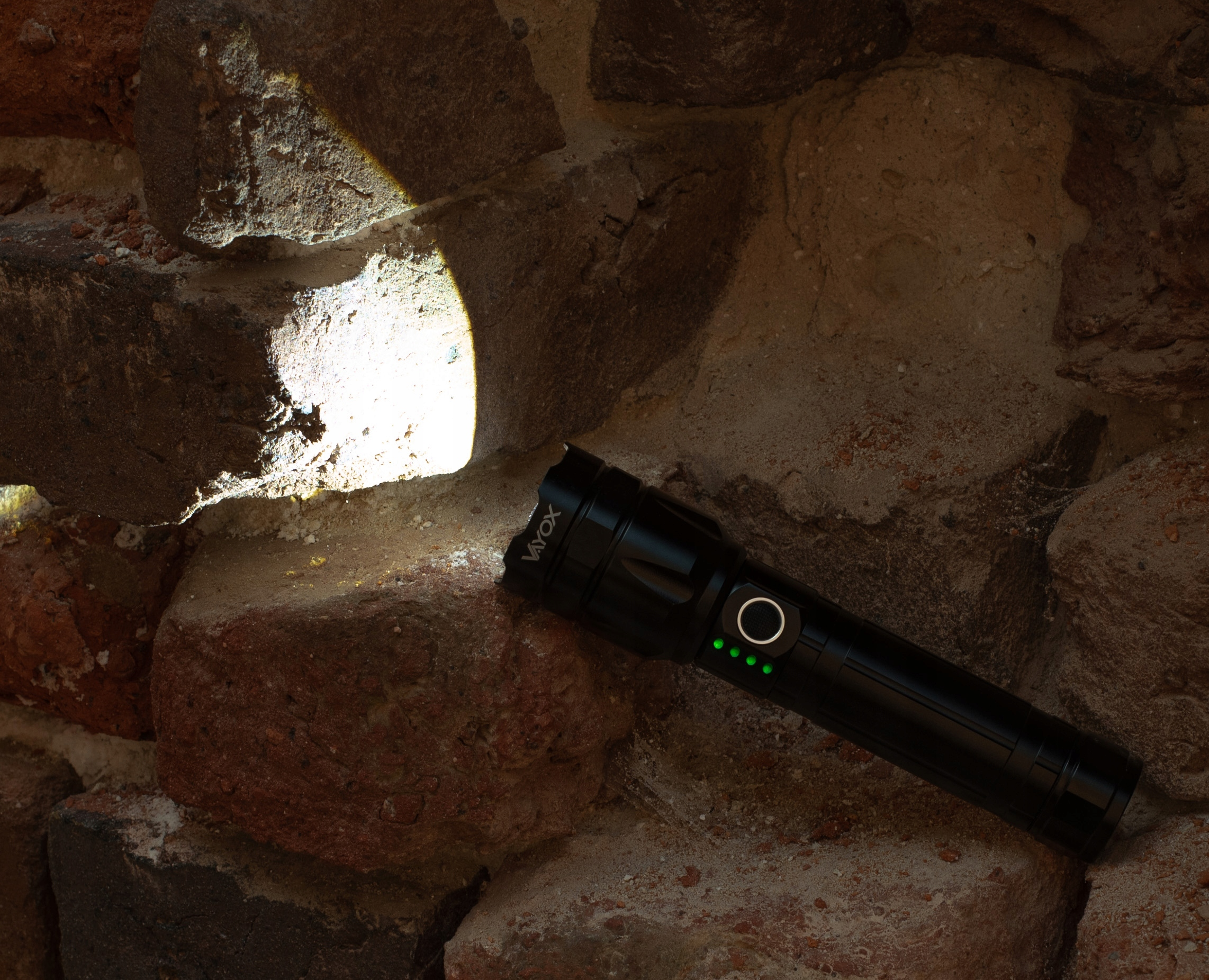 Czarna latarka świecąca wiązką światła na czerwoną ceglaną ścianę. Latarka ma zielone diody LED.