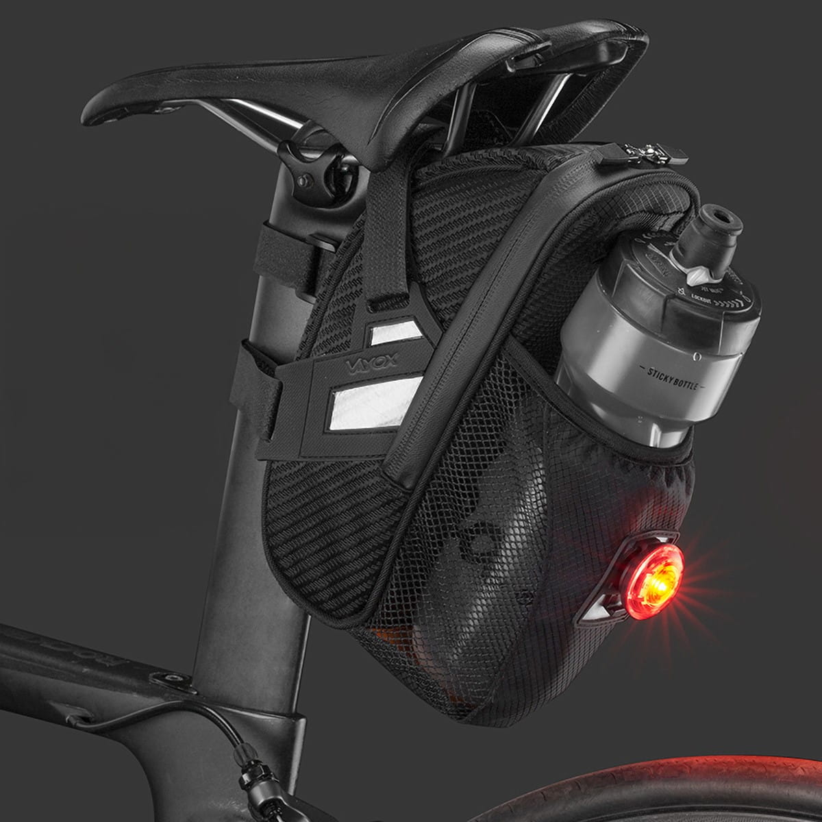 Czarna torba rowerowa z uchwytem na butelkę i czerwonym światłem. Zamontowana na siodełku roweru.