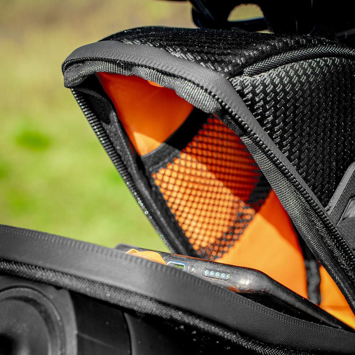 Wewnątrz czarnej torby rowerowej widoczny jest telefon w pomarańczowej siatkowej kieszeni.