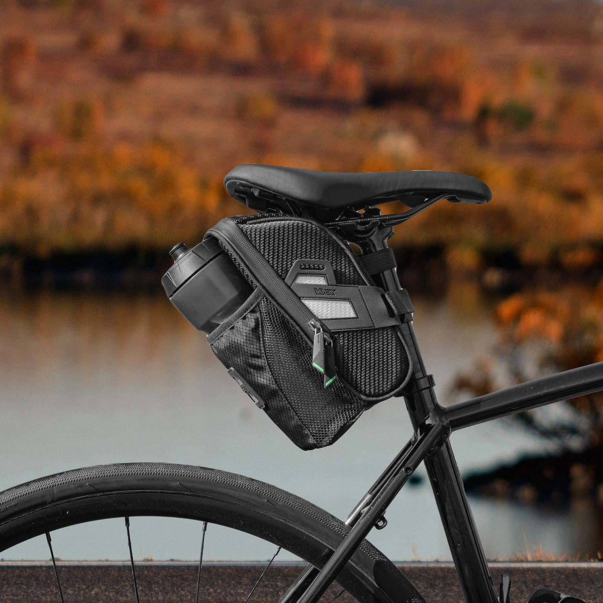 Czarna torba rowerowa przymocowana do sztycy podsiodłowej. Posiada uchwyt na bidon i odblaskowy pasek.