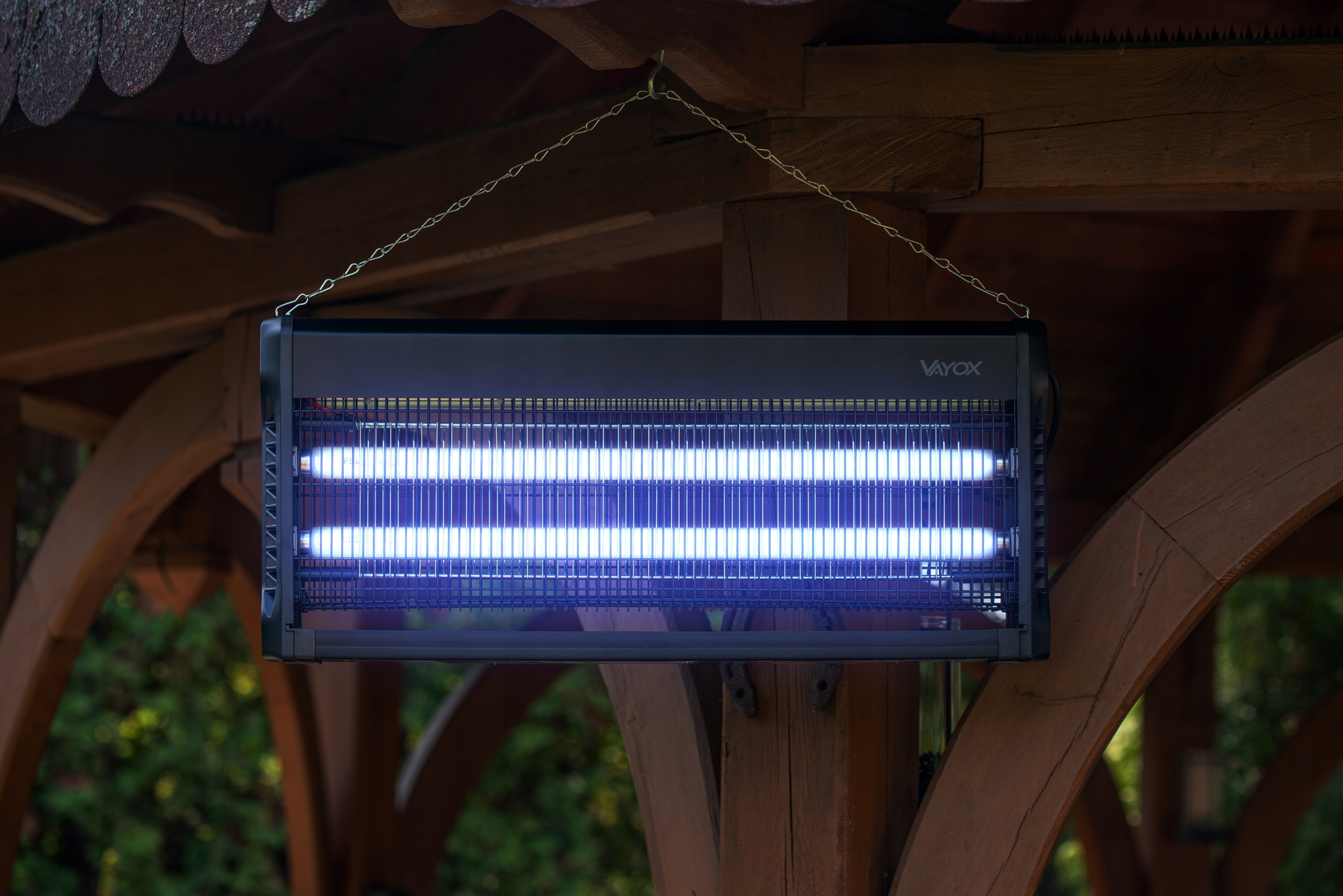 Czarny zabójca owadów zawieszony pod drewnianą konstrukcją. Emituje niebieskie światło.